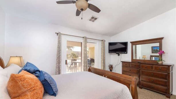 A bedroom with a bed, a ceiling fan, a television, a dresser, and a sliding glass door leading to an outdoor area. - Las Palmas Resort #1638 | All-Inclusive Amenities (Saint George)