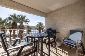 A balcony with a pool, lounge chairs, a table, and a grill.