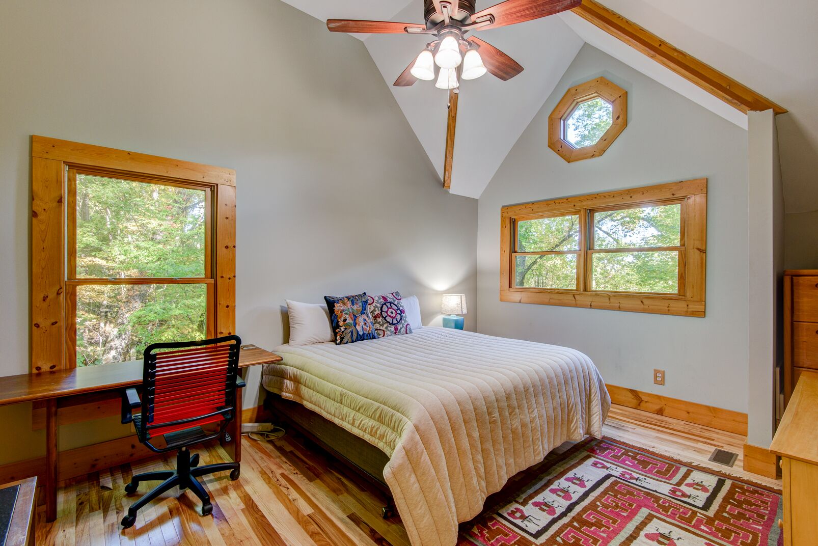 A bedroom with a bed, desk, chair, and two windows.