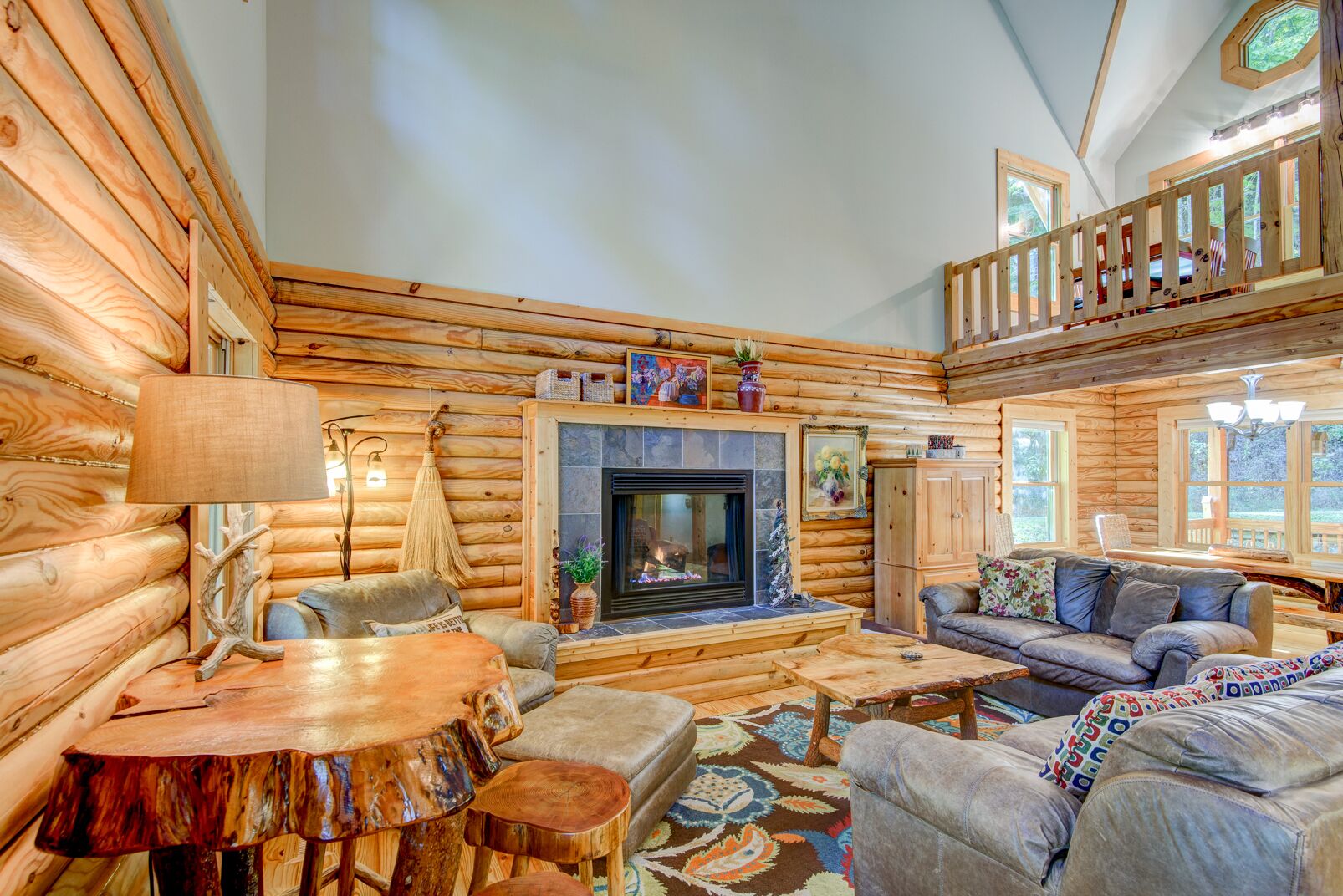 A log cabin interior with a fireplace, wooden furniture, and a balcony.