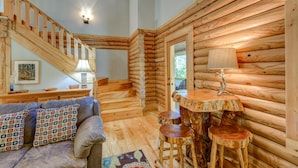 A log cabin interior with a staircase, a sofa with patterned cushions, a table with a lamp, and a rustic wooden chair. - Hideaway Homestead - Private 3BR home between Boone/ Banner Elk! Pet friendly, excellent location! (Banner Elk)