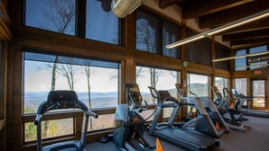 Une salle de sport équipée de tapis de course et d’appareils elliptiques, de grandes fenêtres offrant une vue sur les montagnes et un aménagement intérieur en bois.
