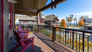 Une terrasse en bois avec des fauteuils Adirondack rouges, un espace couvert doté d’une rambarde, et une vue sur des maisons et des arbres.