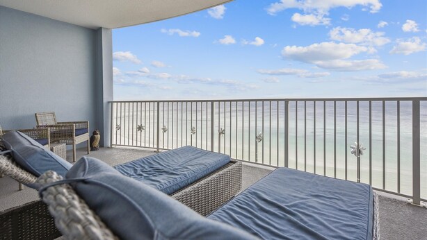 A balcony with wicker furniture and cushions, overlooking a calm sea and clear sky.