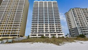 Three high-rise buildings with multiple balconies, a parking structure, and a sandy beachfront.