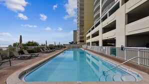 A swimming pool with lounge chairs and a high-rise building in the background.