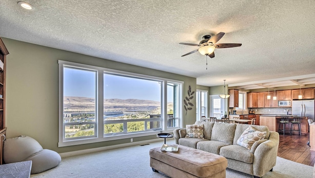 A spacious living room with a large window offering a view of a valley, a ceiling fan, and a kitchen area in the background. - Incredible Oregon Retreat w/ Private Hot Tub! (The Dalles)