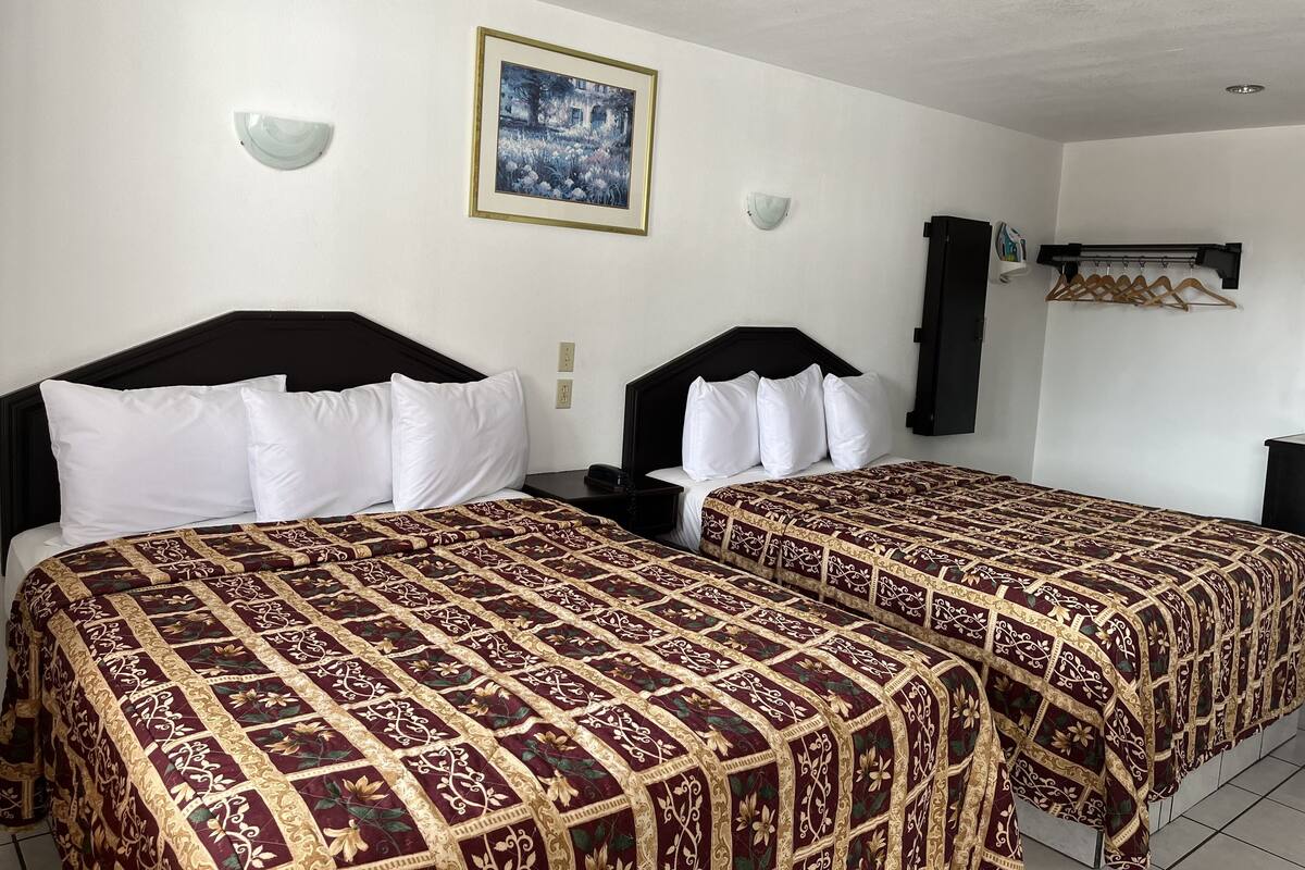 Una habitación de hotel con dos camas, un cuadro enmarcado en la pared y un perchero.