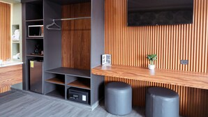 Une chambre moderne dotée d’une armoire intégrée, d’un téléviseur à écran plat fixé sur un mur recouvert de panneaux en bois, et d’une petite table sur laquelle est posée une plante en pot.