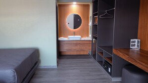 Une chambre d’hôtel moderne équipée d’un lit, d’une coiffeuse avec un miroir, d’un lavabo et d’une armoire.
