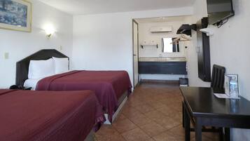 A hotel room with two beds, a desk, a TV, a bathroom with a mirror and sink, and a painting on the wall.
