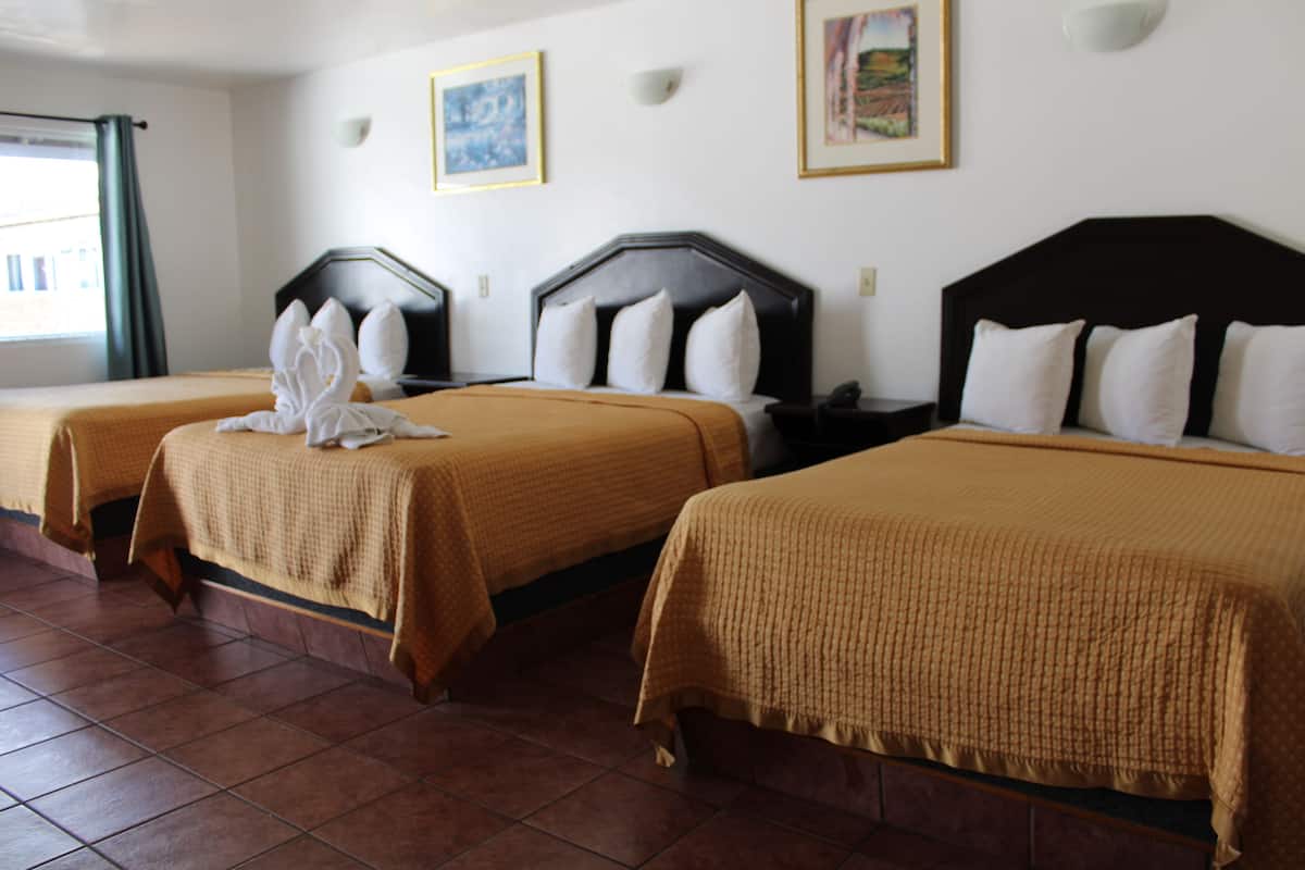 Habitación de hotel con tres camas, cada una con cabecera y almohadas.