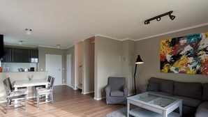 A modern living room with a glass coffee table, grey sofa, and a vibrant abstract painting. - Naturferienhaus 2 - Naturferienhaus auf der Insel Rügen (Poseritz)