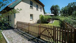 A two-story house with a wooden fence, a patio with outdoor furniture, and a well-maintained garden. - Naturferienhaus 2 - Naturferienhaus auf der Insel Rügen (Poseritz)