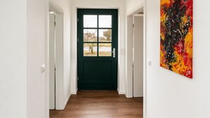 Un pasillo con una puerta verde oscuro, paredes blancas y suelo de madera.