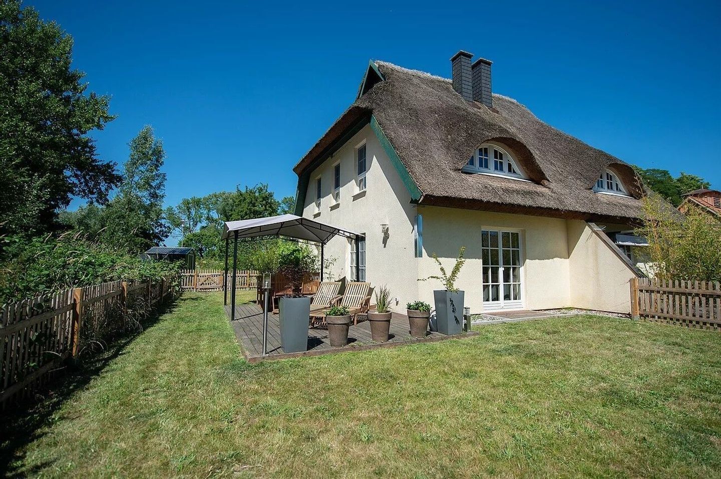 Ein Haus mit Strohdach, überdachter Terrasse und umzäunter Garten.