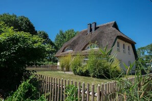 Une maison avec un toit de chaume, une clôture en bois et une végétation luxuriante.