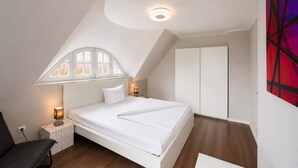 Un dormitorio con cama, mesita de noche, silla, armario y una lámpara en el techo.