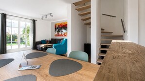 Una sala de estar moderna con una mesa de madera, sillas azules, un sofá y una escalera.