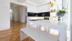 A modern kitchen with white cabinetry, a black countertop, and a bench. There is a window with a view of the outside. - Your comfy stay in Central Sarajevo (Sarajevo)