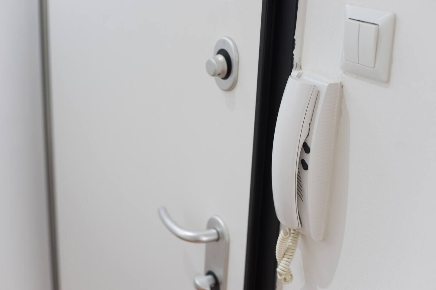 Une porte blanche avec une poignée argentée, un trou de serrure et un système d’interphone blanc.