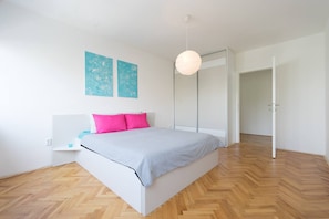 Quarto moderno com cama, mesa de cabeceira, luminária suspensa e guarda-roupa.