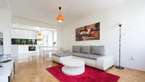 A modern living room with a white sofa, a red rug, and a kitchen in the background. - Your comfy stay in Central Sarajevo (Sarajevo)
