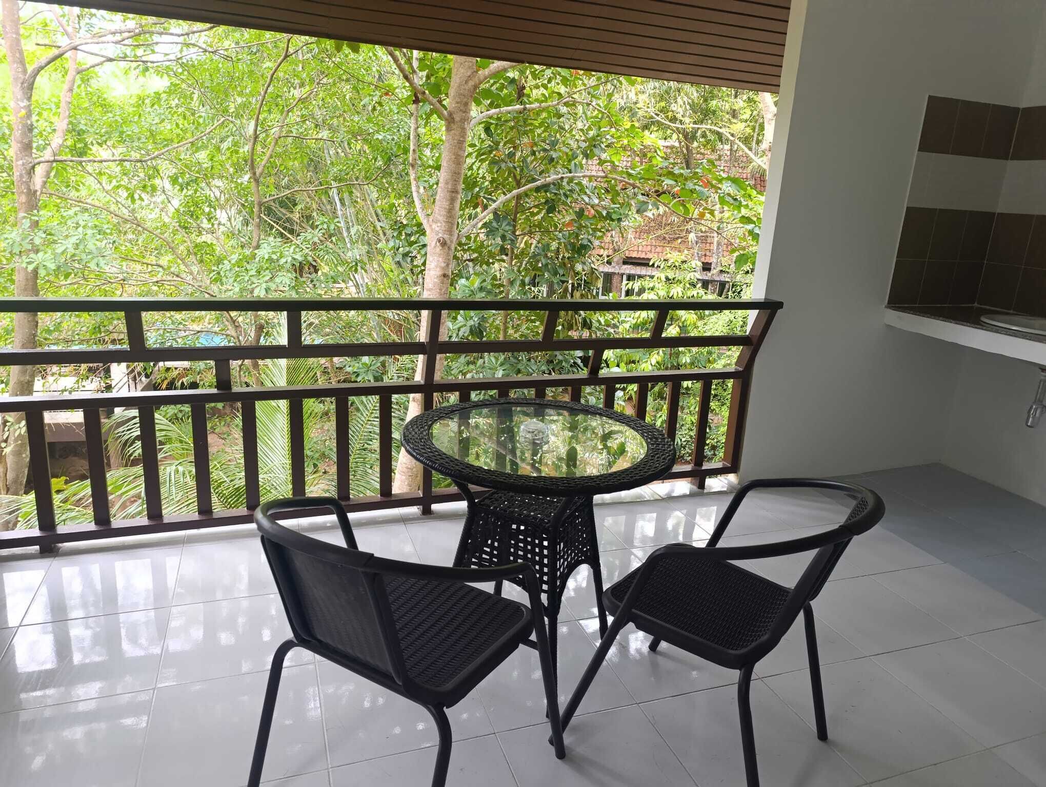Un balcone con un tavolo di vetro e due sedie, affacciato su un rigoglioso giardino.