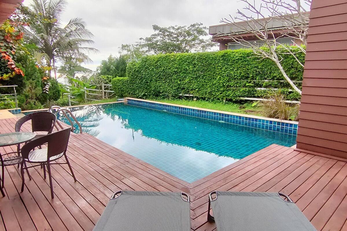 Um deck de madeira com piscina, rodeado por vegetação e uma cadeira suspensa.