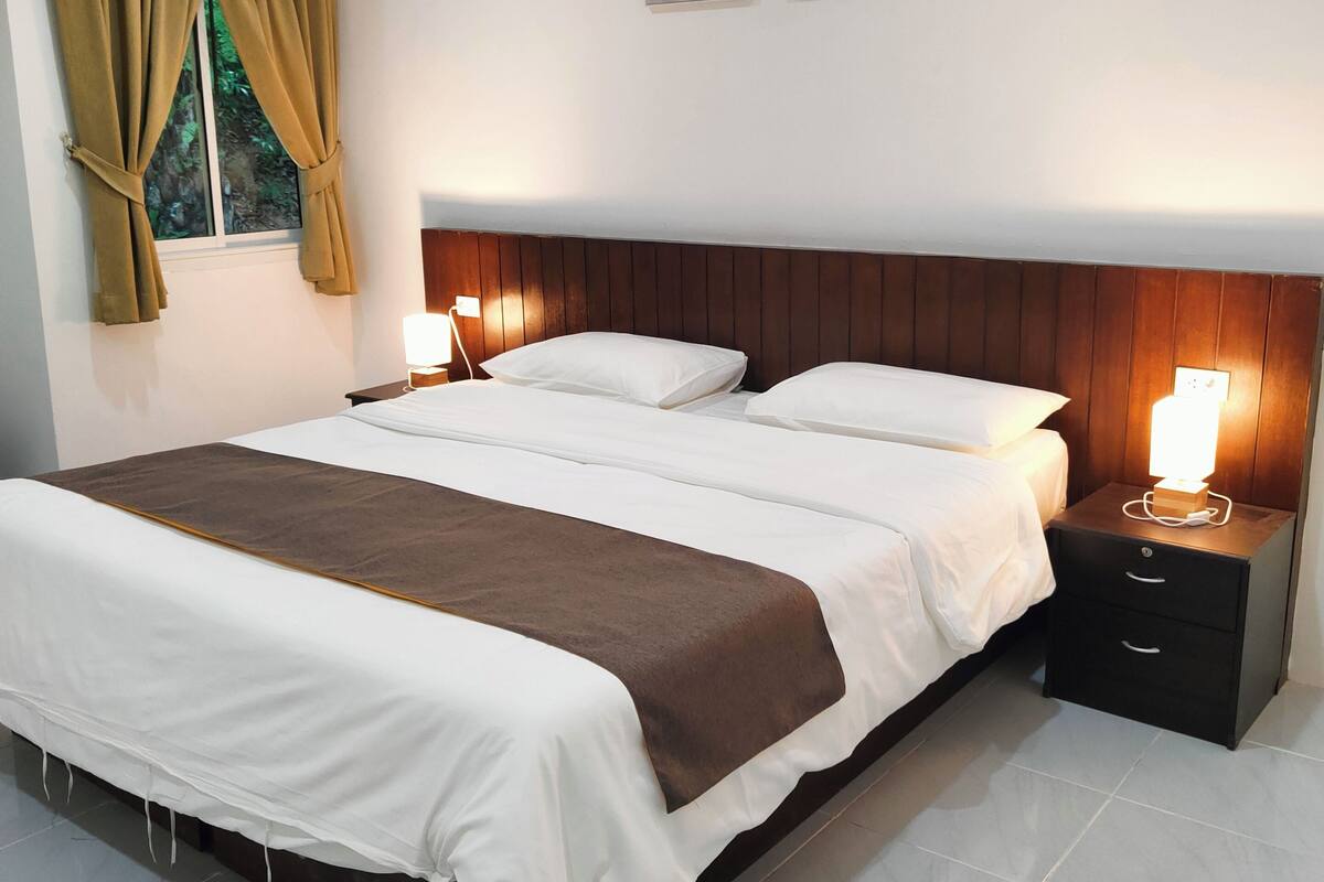 Quarto com uma cama grande, duas mesas de cabeceira com luminárias, uma cabeceira de madeira e dois quadros de flores na parede.