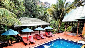 A swimming pool with lounge chairs and umbrellas, surrounded by lush greenery. - Phuket Jungle Experience Resort (Karon)