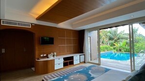 A modern bedroom with a large bed, a TV, a desk, and a view of a pool. - Phuket Jungle Experience Resort (Karon)