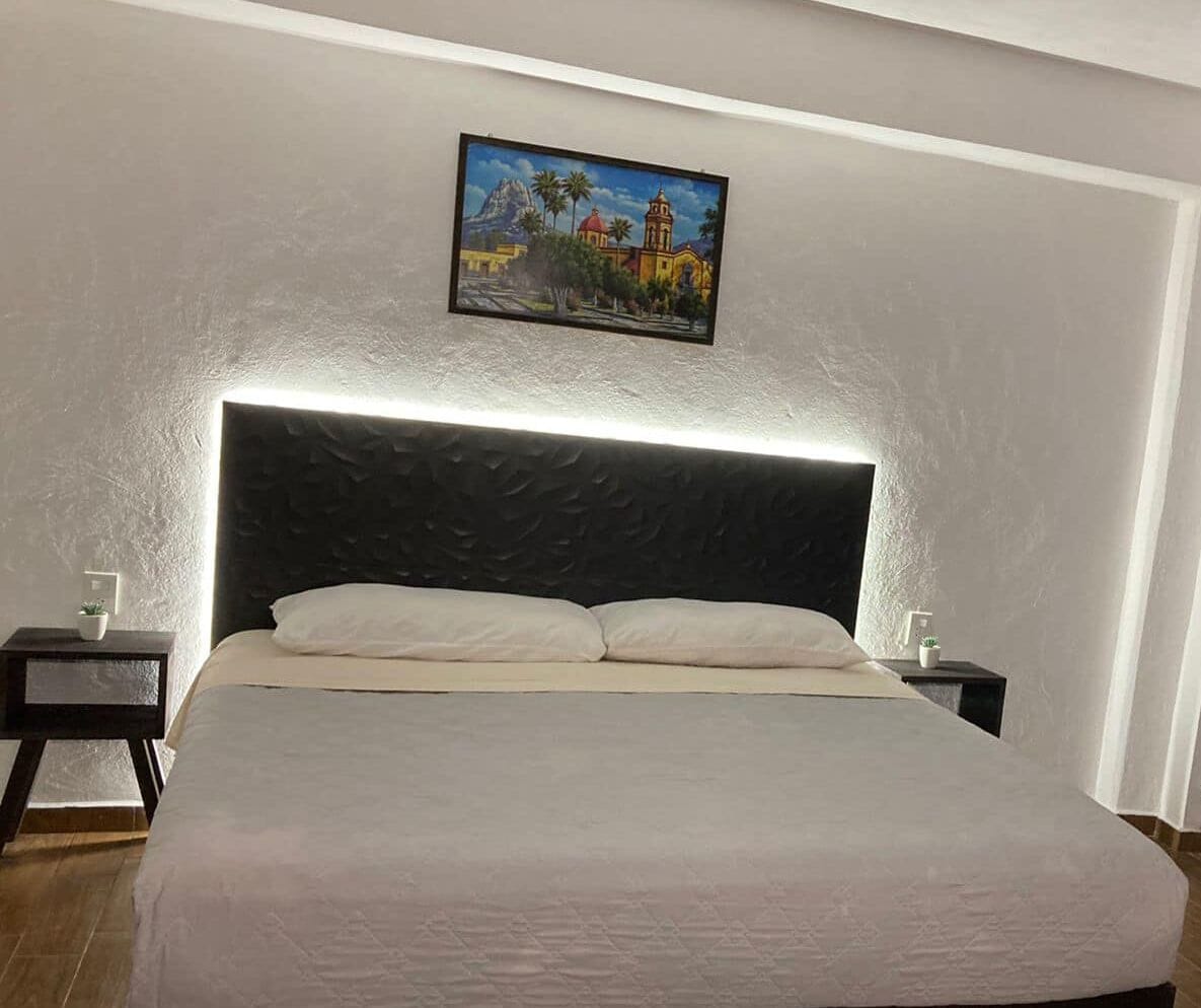 Een slaapkamer met een groot bed, twee nachtkastjes, een aan de muur hangend schilderij en een gestructureerd hoofdbord.