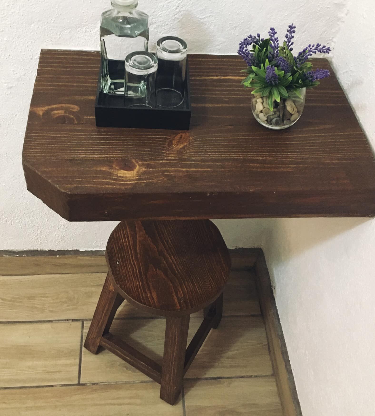 A wooden table with a stool underneath, a small potted plant, and a tray with candles and a bottle.