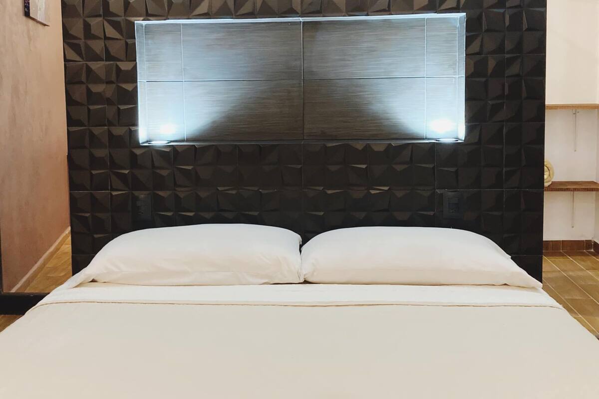 A bed with a headboard featuring a geometric pattern and a flat, light-colored mattress.