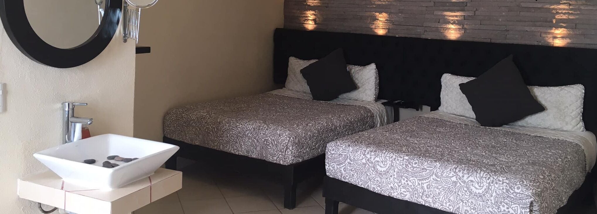 Habitación de hotel con dos camas, un lavamanos blanco y un espejo.