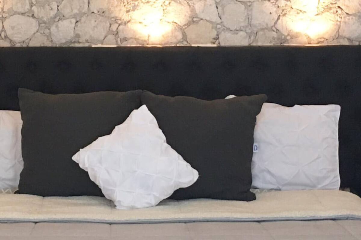 A bed with a black headboard, white and dark pillows, and a stone wall background.