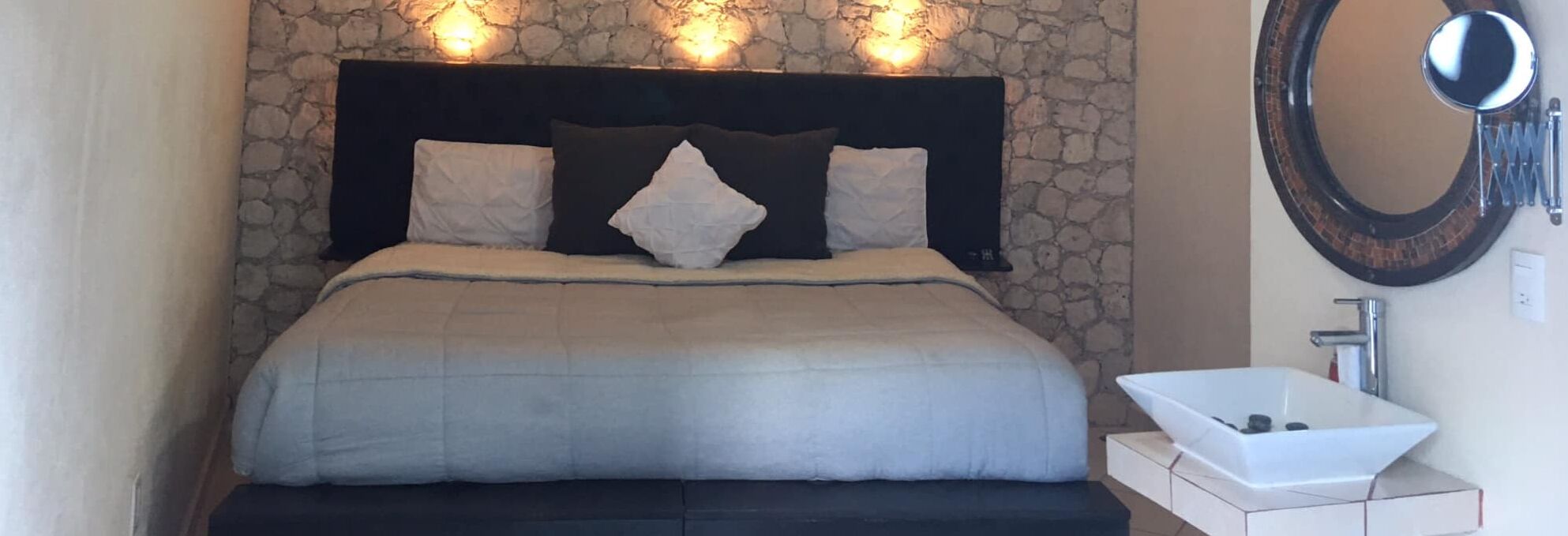 A bedroom with a stone wall, a bed with a dark headboard, and a white sink.