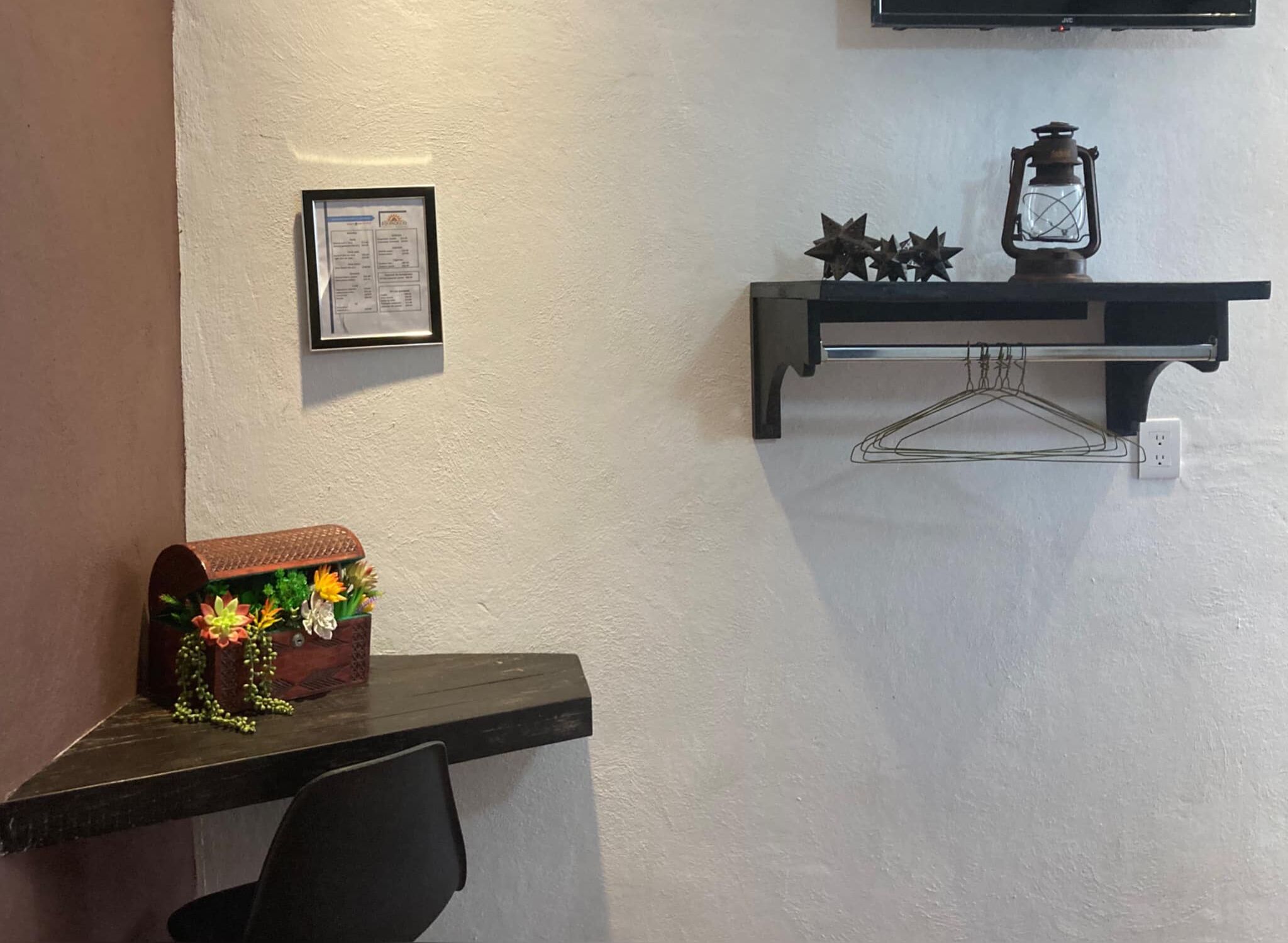 Una habitación con un escritorio, un certificado en un marco en la pared, una estantería con un farol y adornos con forma de estrella, y una pequeña planta con flores.