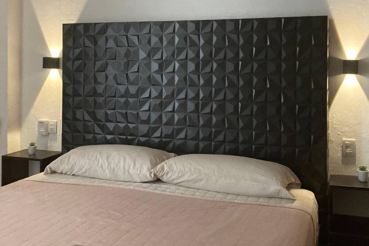 A modern bedroom with a geometric-patterned headboard, two bedside tables with lamps, and a large bed with two pillows.