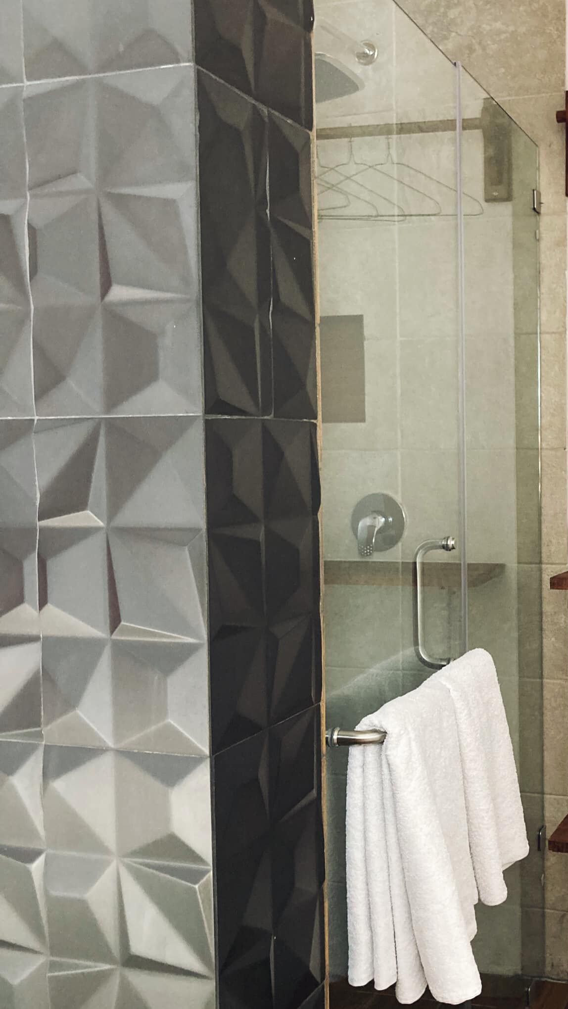 A bathroom with a geometric tile backsplash, a glass shower enclosure, and a towel rack with a white towel.