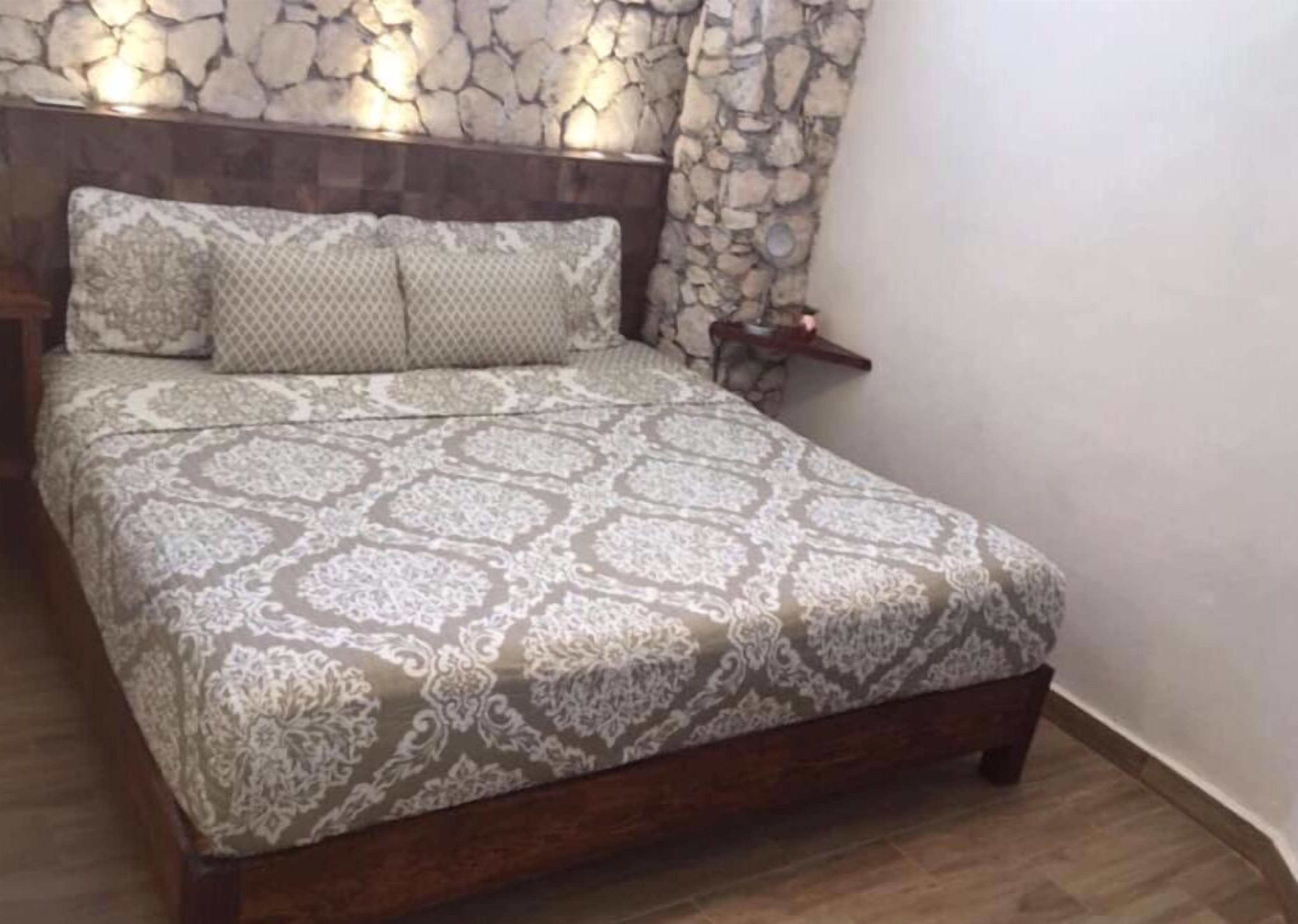 A bedroom with a patterned bedspread, a wooden headboard, and a stone wall.