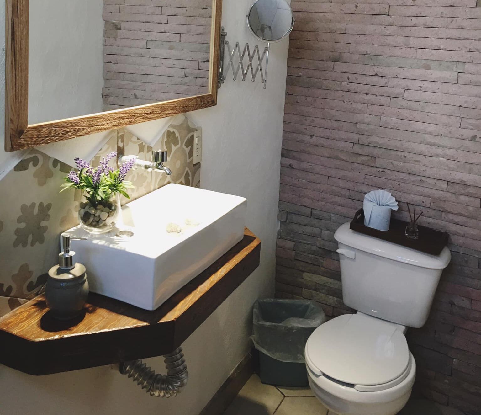 Un baño con un lavamanos blanco, un espejo, un inodoro y un cesto de basura.
