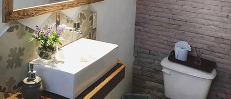 Un baño con un lavamanos blanco, un espejo, un inodoro y un cesto de basura.