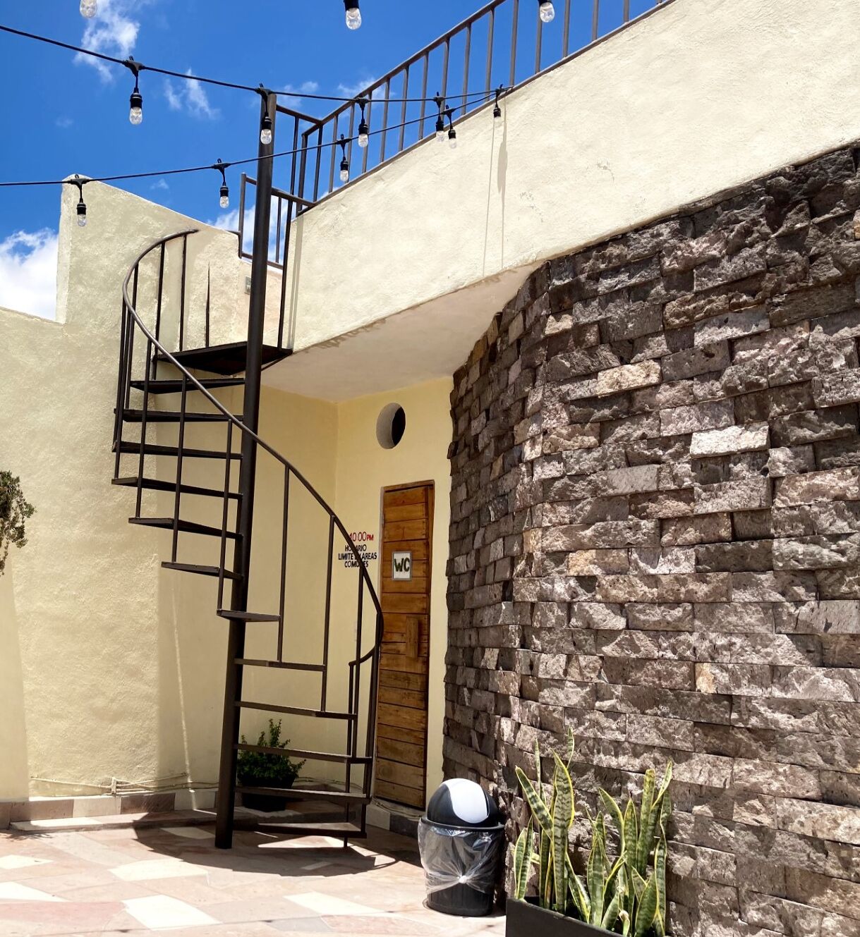 Escadaria em espiral que leva a um segundo andar, parede de pedra, porta de madeira com a inscrição 