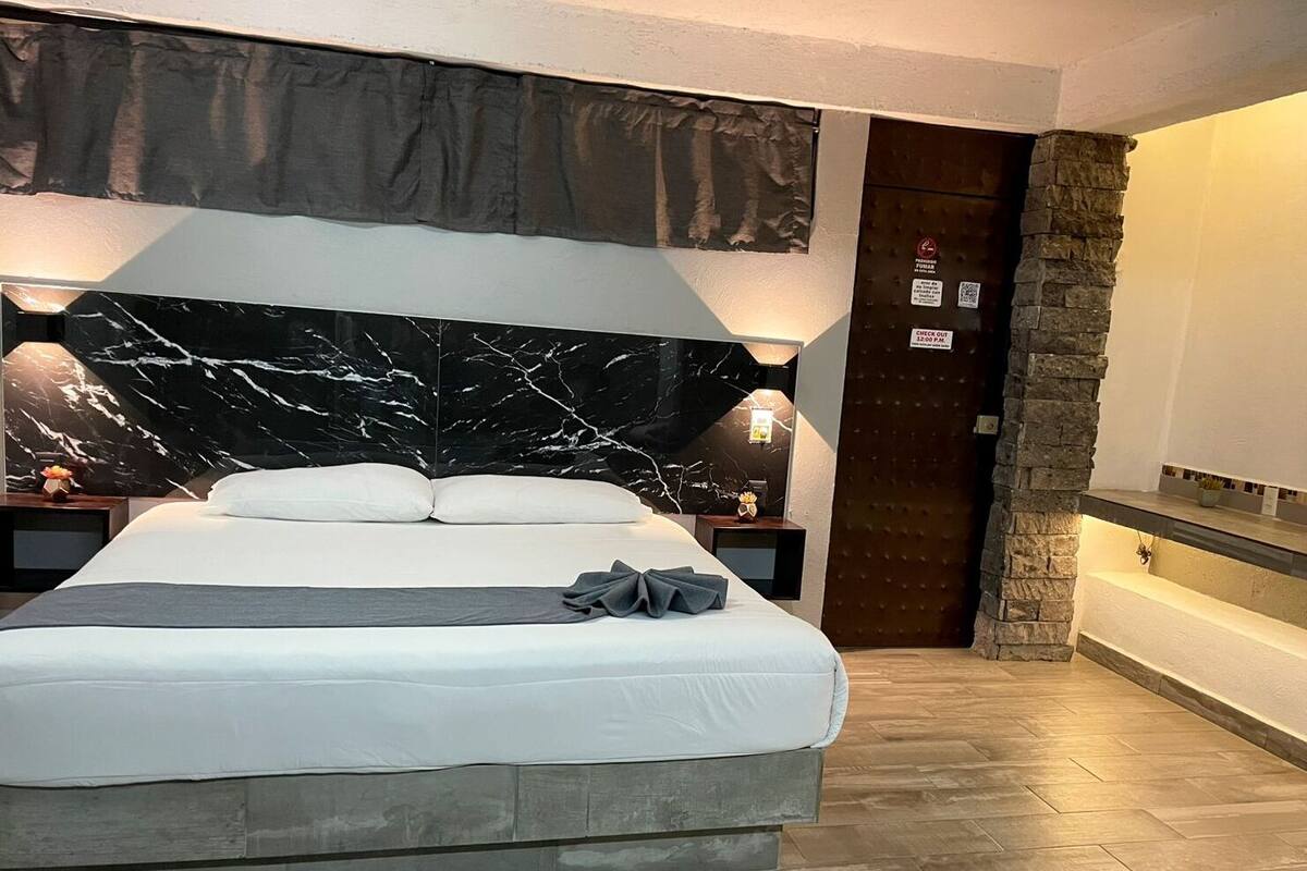 A modern hotel room with a large bed, marble headboard, and a stone accent wall.