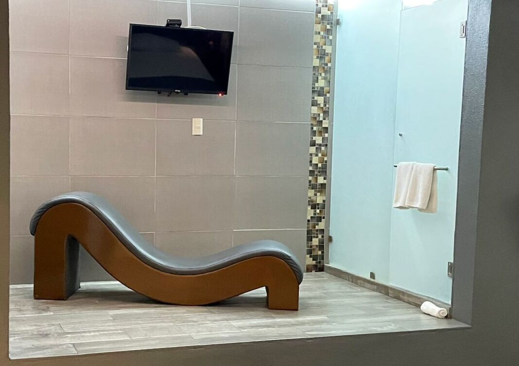 A modern bathroom with a curved bench, a flat-screen TV mounted on the wall, and a tiled shower area.