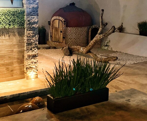 Un sendero de piedra conduce a un edificio rústico con techo abovedado, rodeado de un jardín ajardinado con una jardinera de plantas verdes.