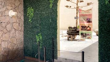 A stone wall with a green hedge, an archway leading to a shop, and a wooden cart with items.