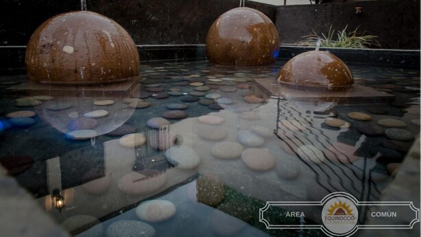 A tranquil water feature with three spherical fountains in a stone-lined pool, surrounded by a modern building facade. - Equinoccio Peña de Bernal (Ezequiel Montes)